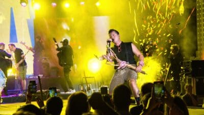 Andreas Gabalier singt auf einer gelb beleuchteten Bühne mit Konfetti und Publikum im Vordergrund.