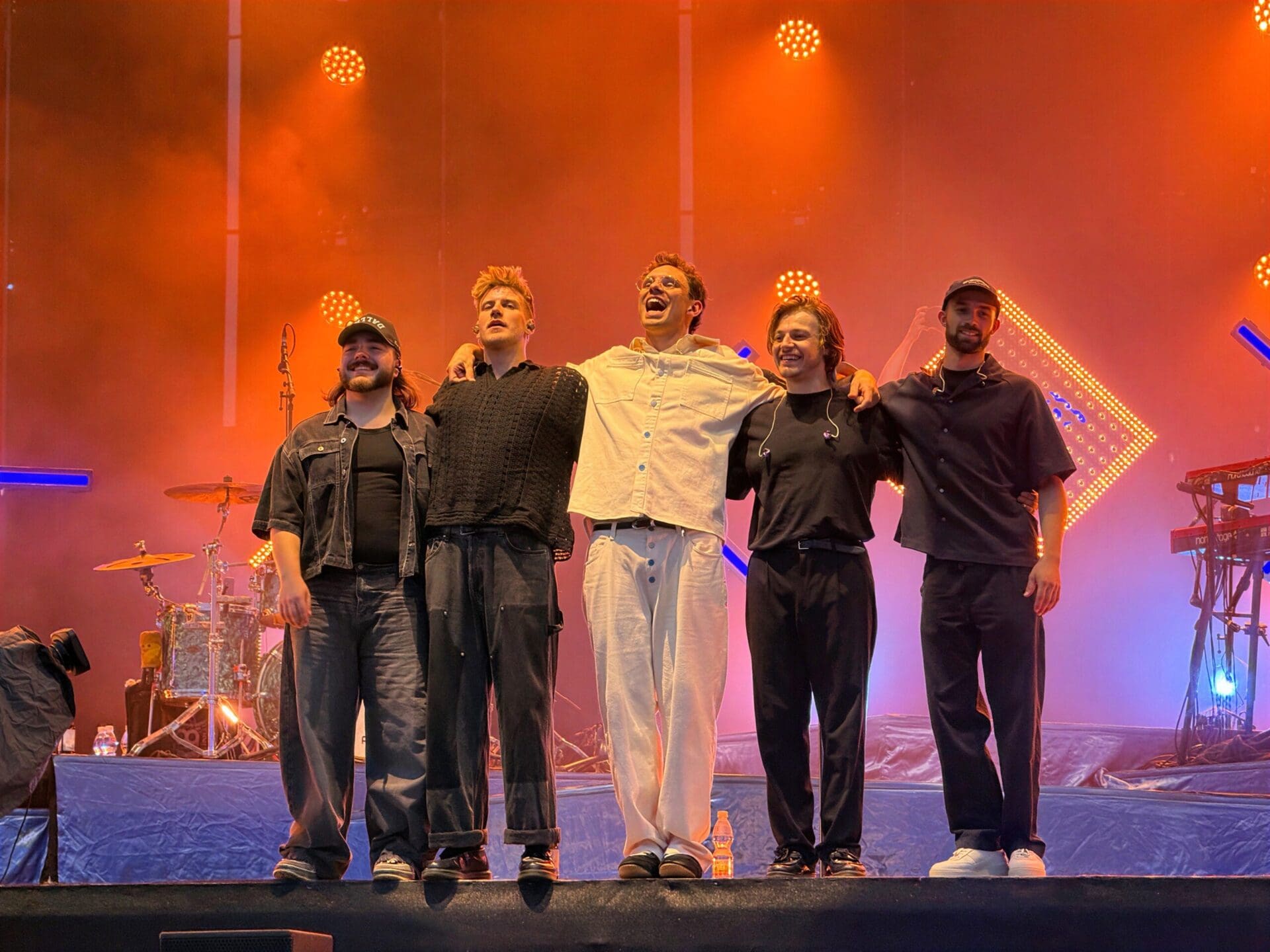 Fünf Musiker stehen eng beieinander auf einer orangefarben beleuchteten Bühne.
