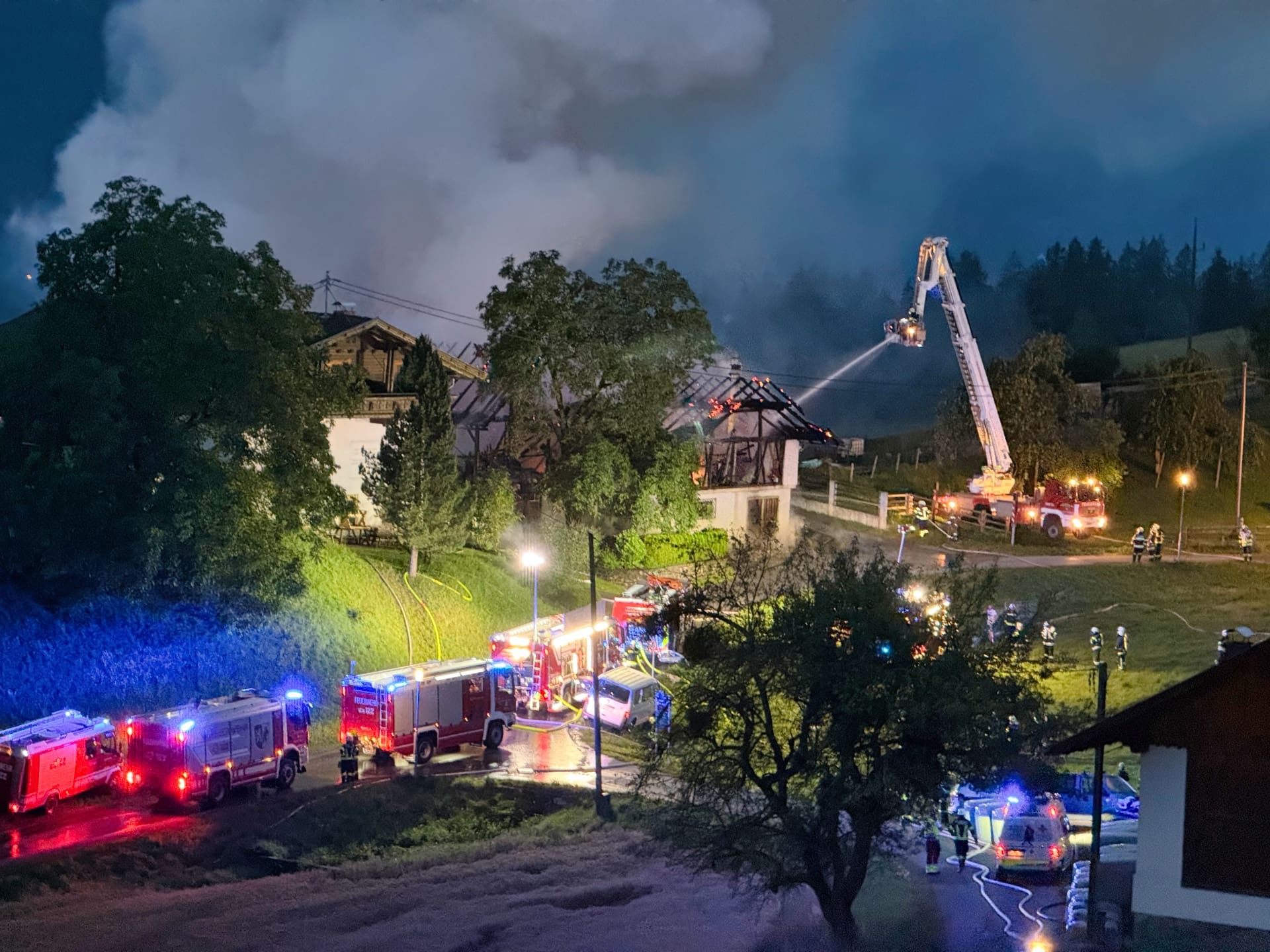 Feuerwehrleute bekämpfen den Brand eines Wirtschaftsgebäudes mit einer Drehleiter bei Nacht.