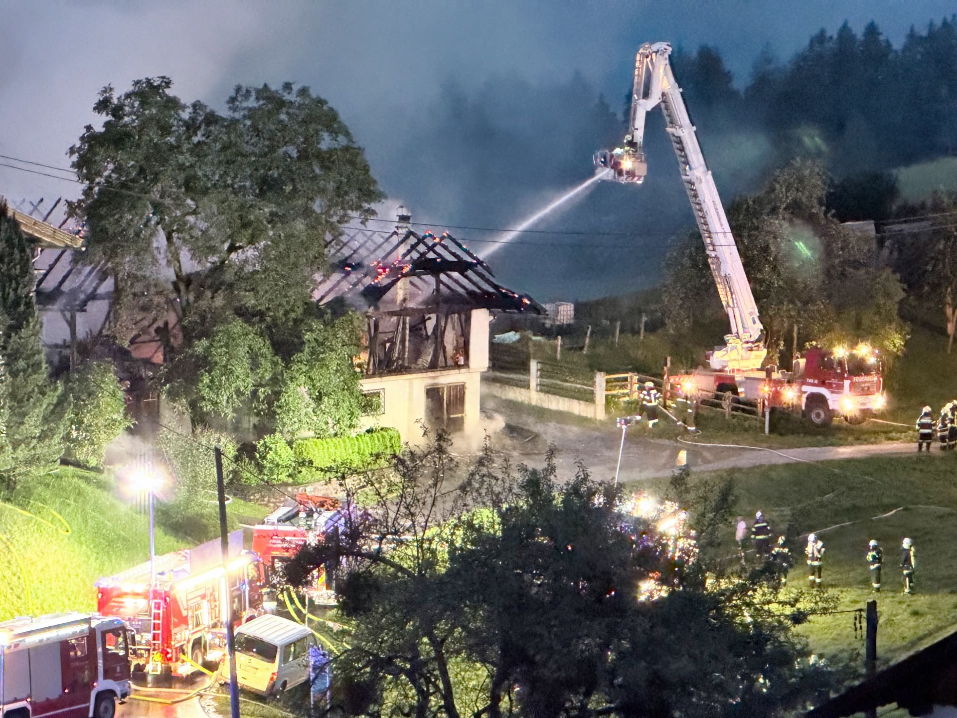Drehleiter der Feuerwehr spritzt Wasser auf brennendes Wirtschaftsgebäude bei Nacht in Irschen