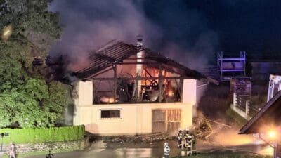 Feuerwehrkräfte löschen brennendes Wirtschaftsgebäude mit Flammen und Rauch bei Nacht in Irschen