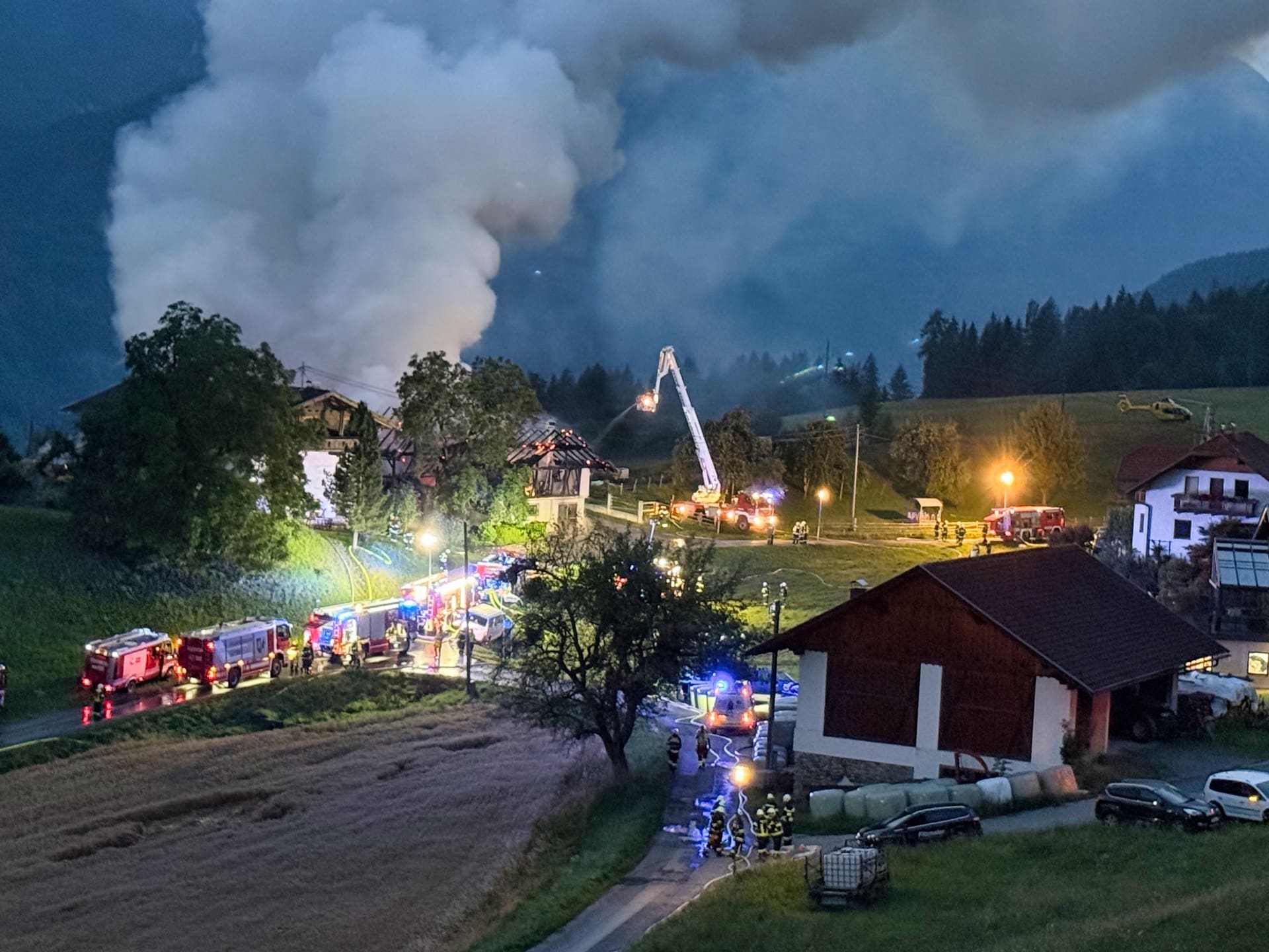 Feuerwehrleute bekämpfen mit Drehleiter und Hubschrauber einen nächtlichen Großbrand eines Wirtschaftsgebäudes in Irschen.