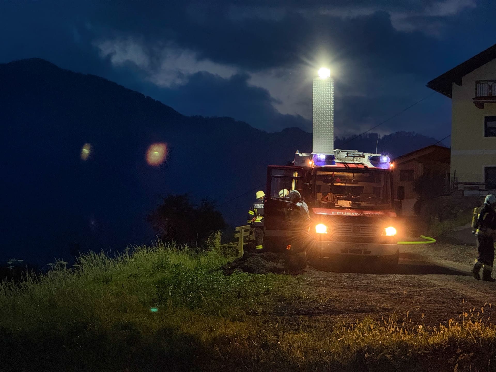 Feuerwehrfahrzeug mit leuchtendem Mast und Blaulicht bei Nacht vor Berglandschaft