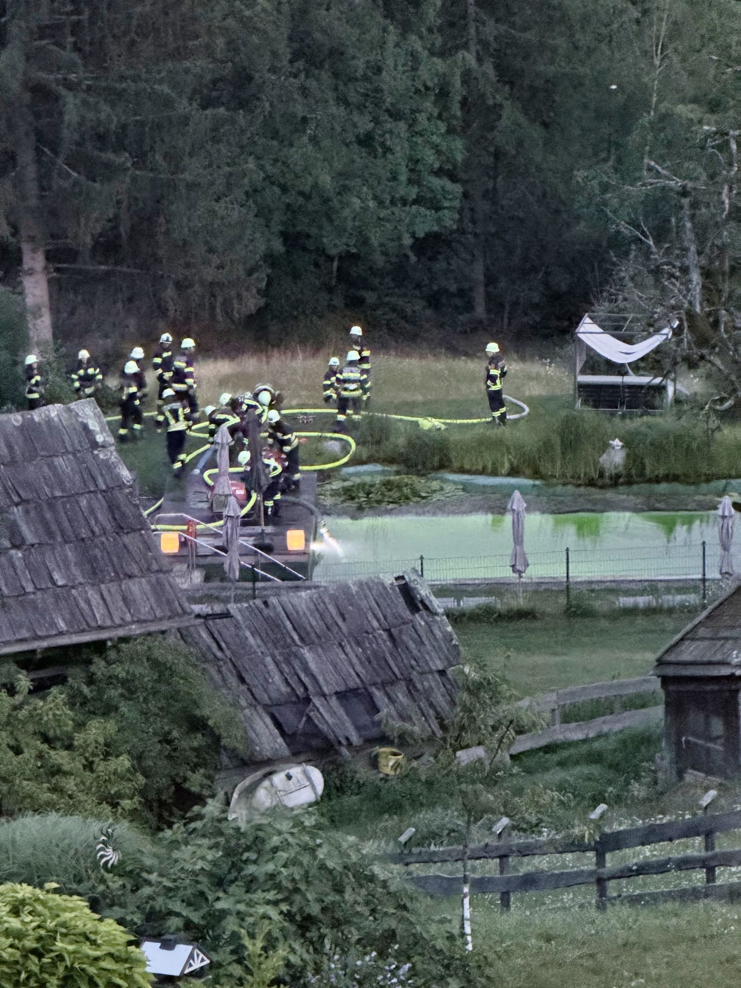 Feuerwehrleute in Einsatzkleidung bedienen eine Pumpe am Rand eines Teichs