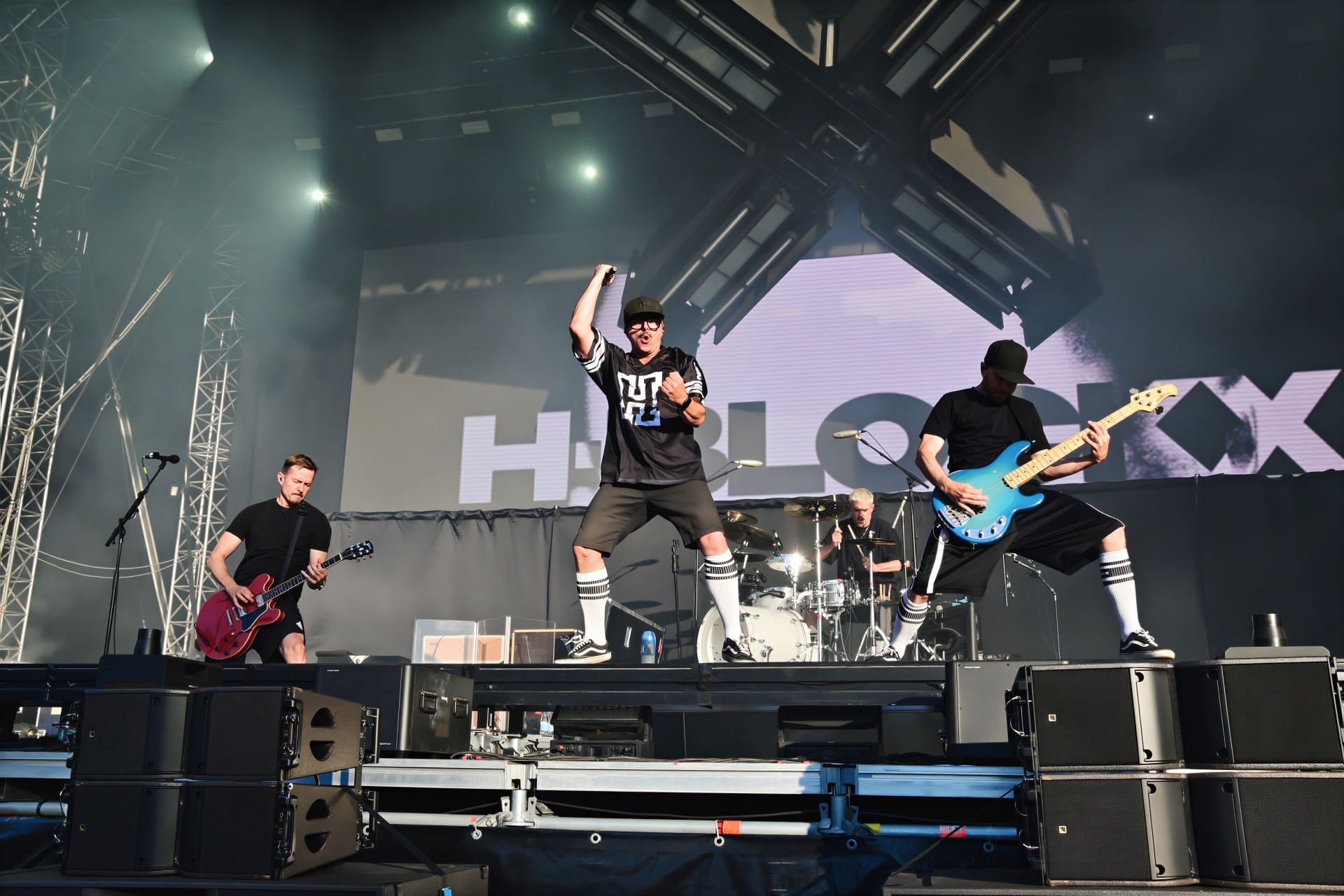 Drei Musiker von H-Blockx auf der Bühne mit roter Gitarre, springendem Sänger und blauer Bassgitarre.