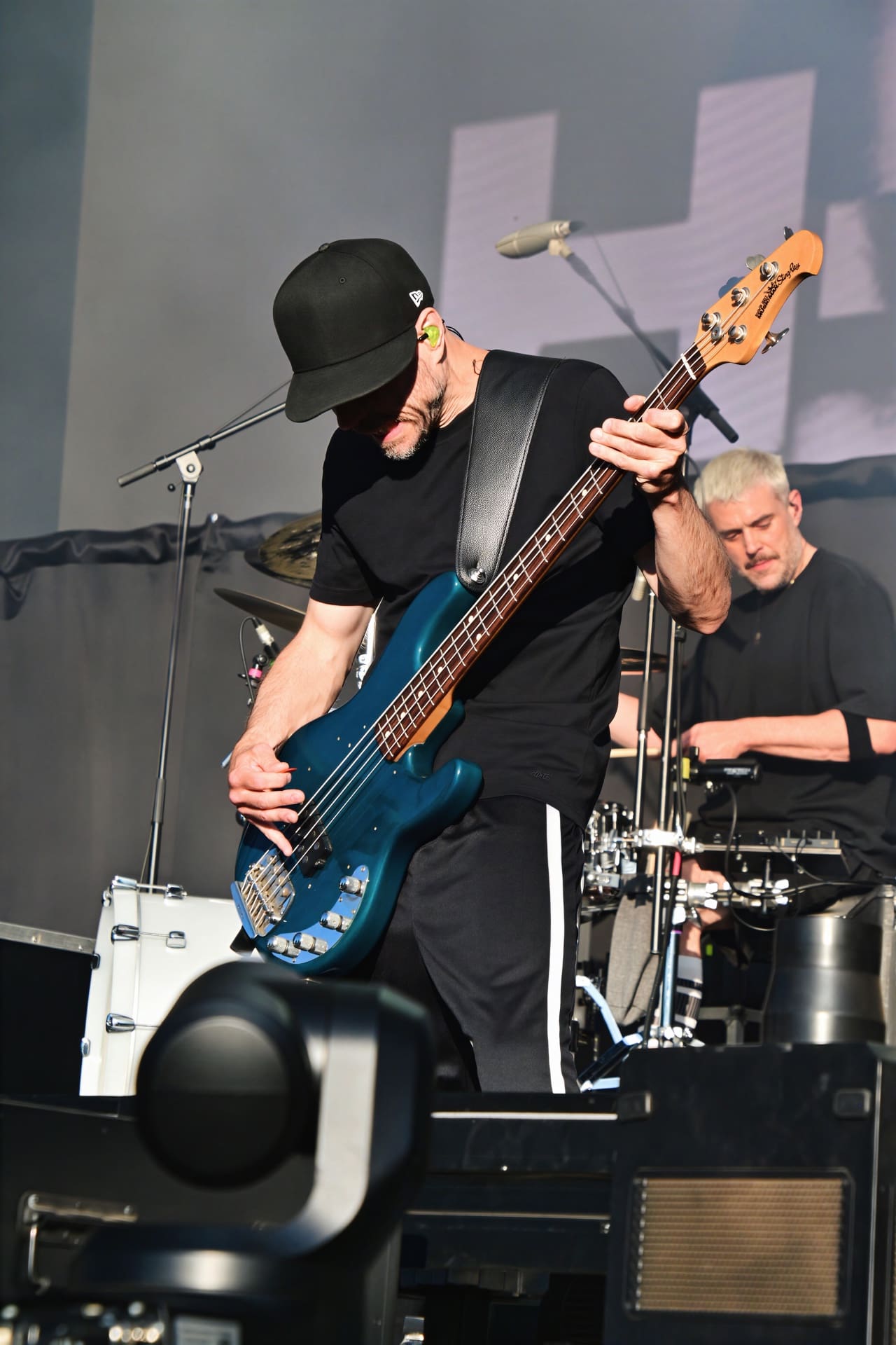 Bassist mit schwarzer Kappe spielt auf einer blauen Bassgitarre bei einem Konzert auf der Bühne.