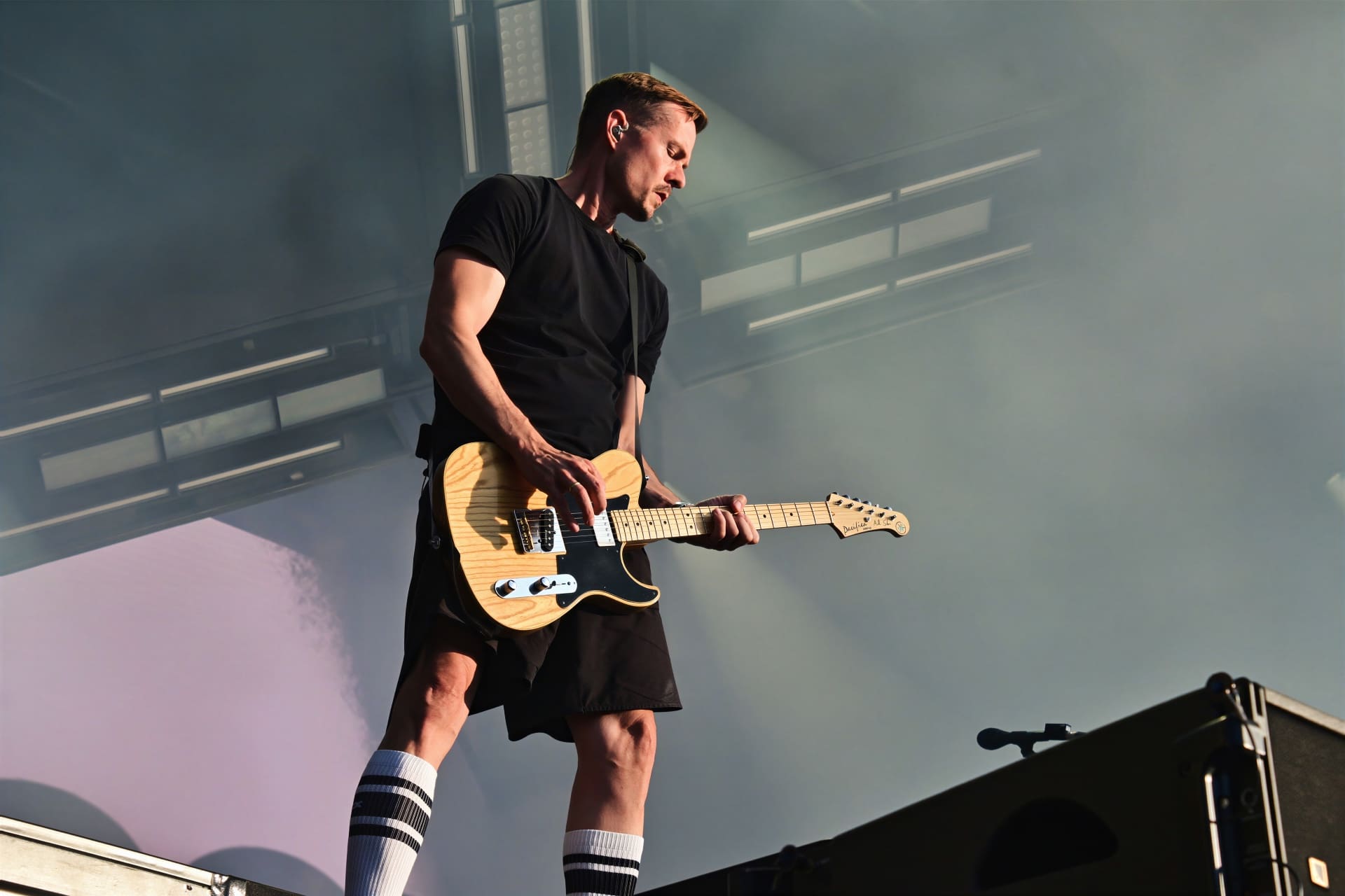 Ein Gitarrist in schwarzem T-Shirt spielt E-Gitarre auf einer Bühne mit Bühnennebel.