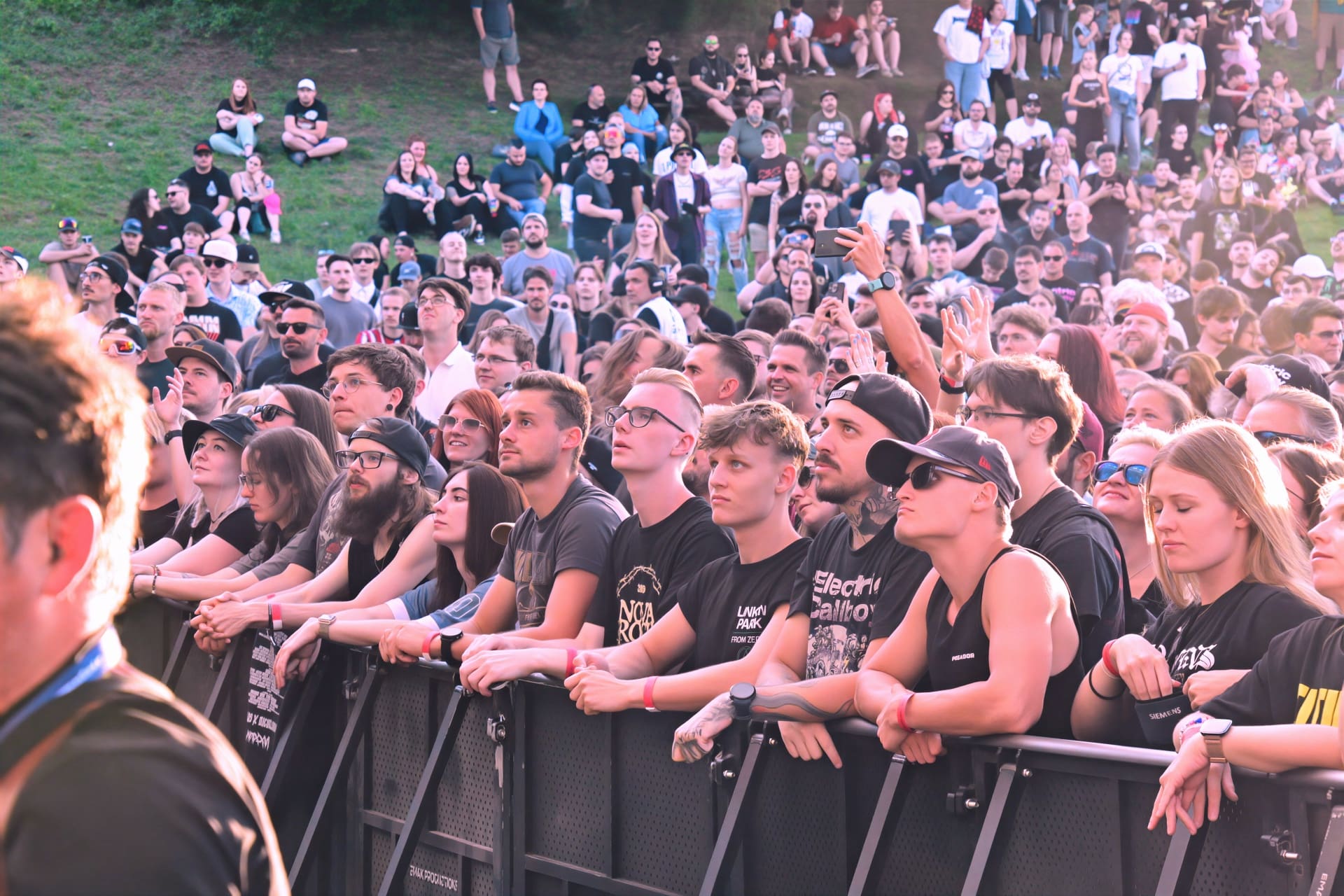 Zuschauer in schwarzen T-Shirts lehnen an einer Barriere beim Konzert auf der Schlosswiese.