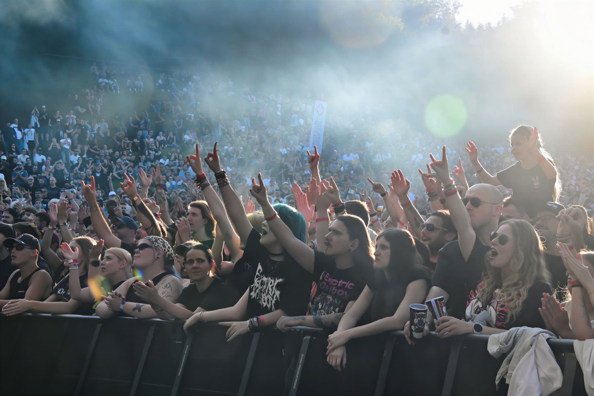 Zahlreiche Konzertbesucher recken bei einem Open-Air-Konzert die Arme in die Höhe und zeigen das Hornzeichen.