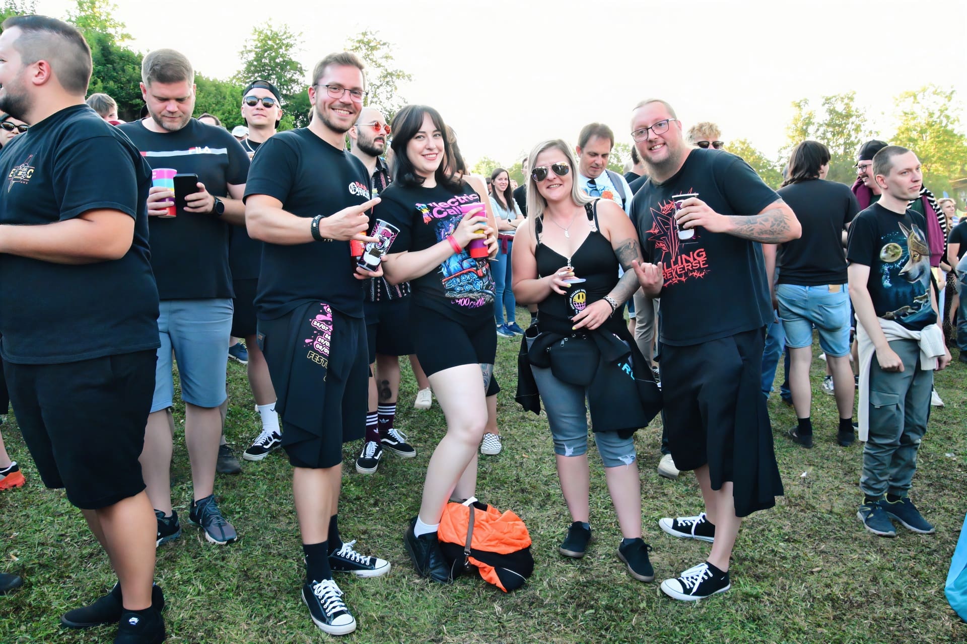 Gruppe junger Menschen in schwarzen Band-Shirts posiert auf einer Wiese bei einem Konzert