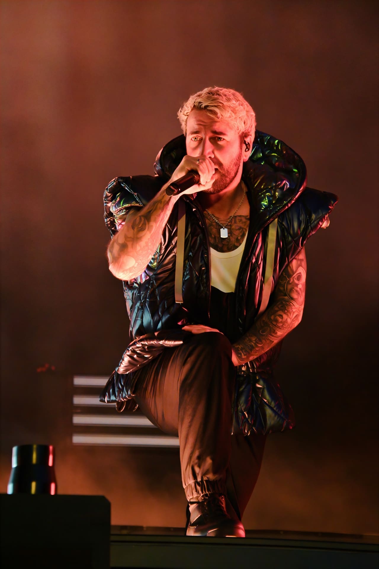 Blonder Sänger mit Tattoos kniet auf der Bühne und singt in ein Mikrofon.