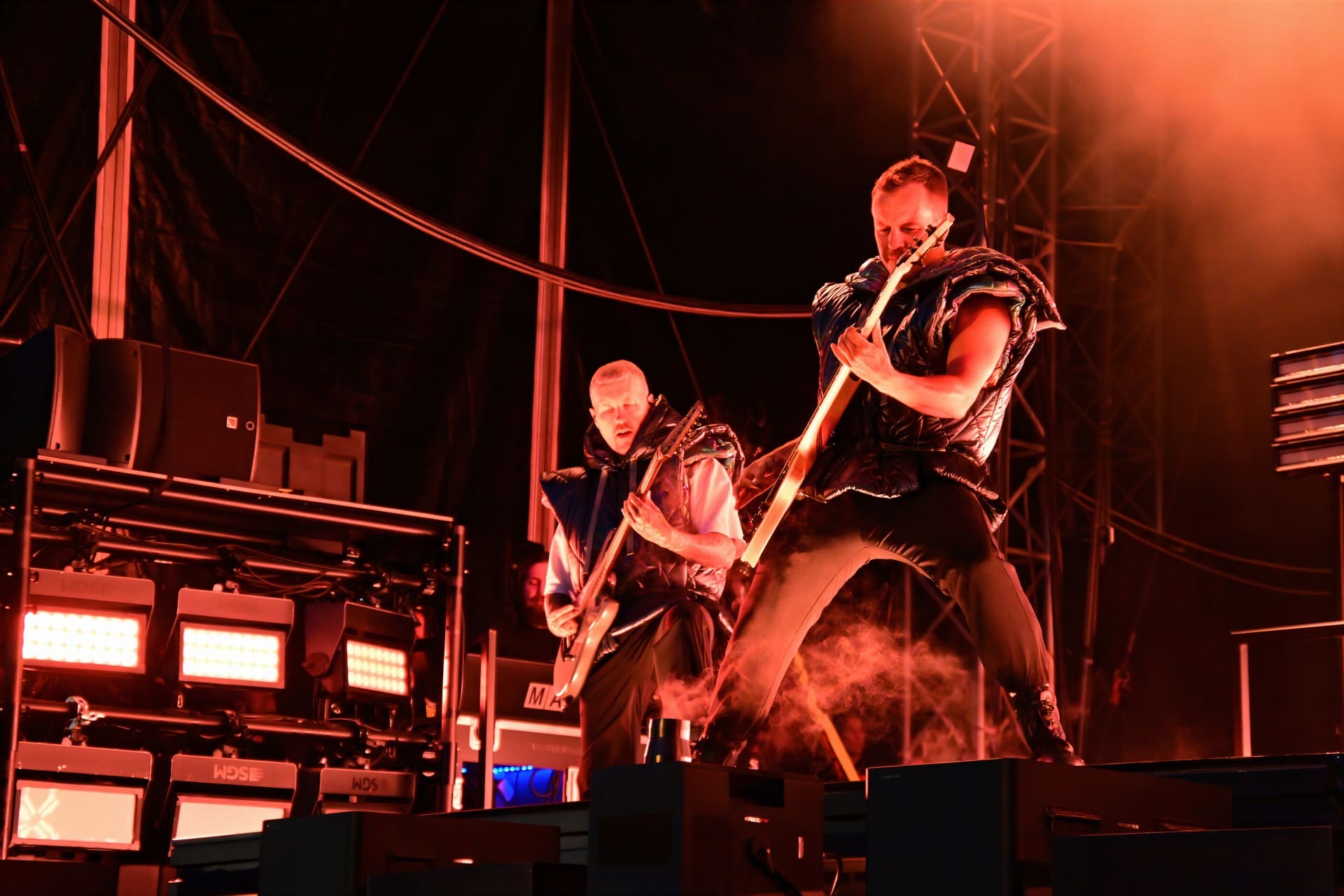 Zwei Gitarristen der Band Electric Callboy spielen auf einer Konzertbühne mit rotem Licht und Nebel.