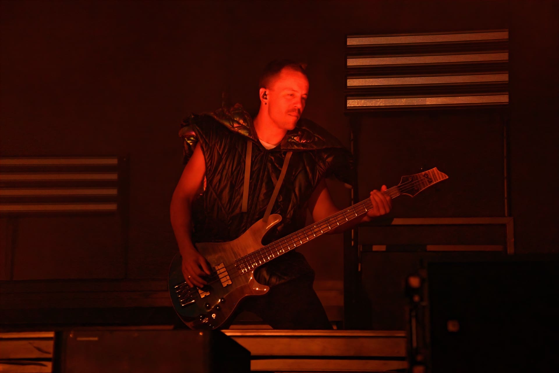 Ein Bassist in schwarzer Weste spielt E-Bass auf der Bühne unter rotem Licht.
