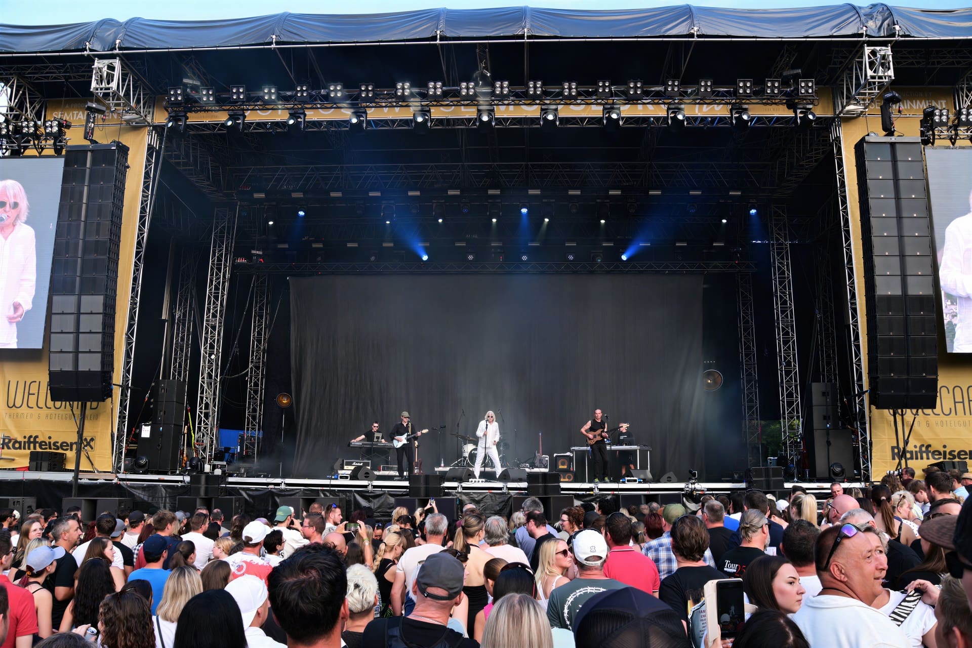 Große Konzertbühne mit Musikern unter Scheinwerfern und dichtem Publikum im Vordergrund auf der Schlosswiese.