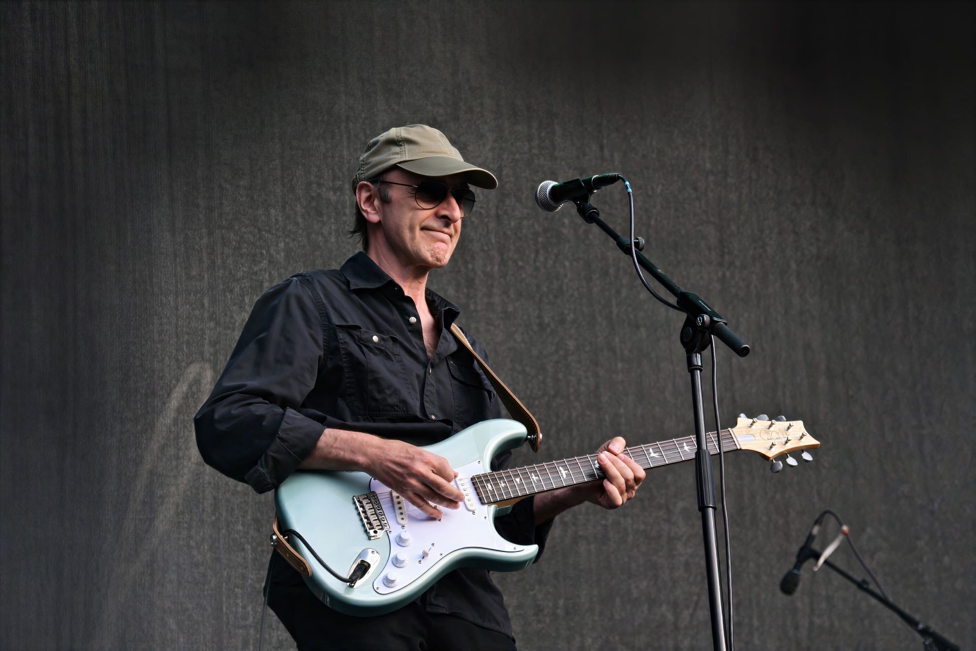 Ein Gitarrist mit Kappe und Sonnenbrille spielt eine hellblaue E-Gitarre auf der Bühne.