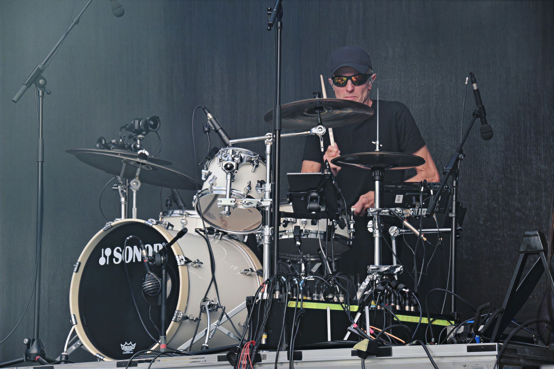 Ein Schlagzeuger mit schwarzer Kappe und Sonnenbrille spielt auf einem weißen Sonor-Schlagzeug auf der Bühne.