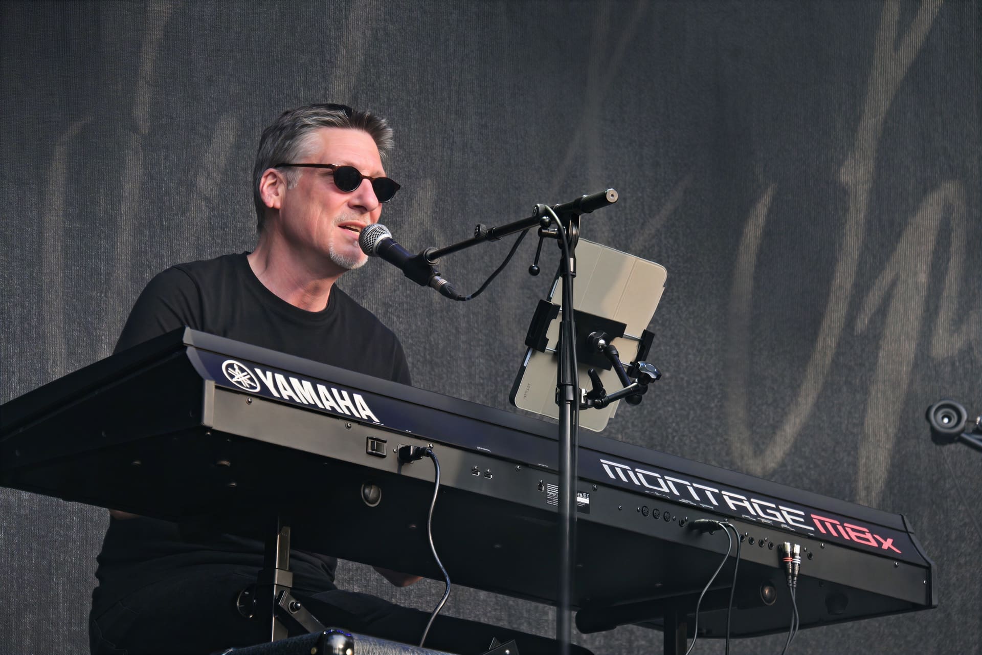 Ein Mann mit Sonnenbrille und grauen Haaren spielt auf einem Yamaha Keyboard und singt ins Mikrofon.