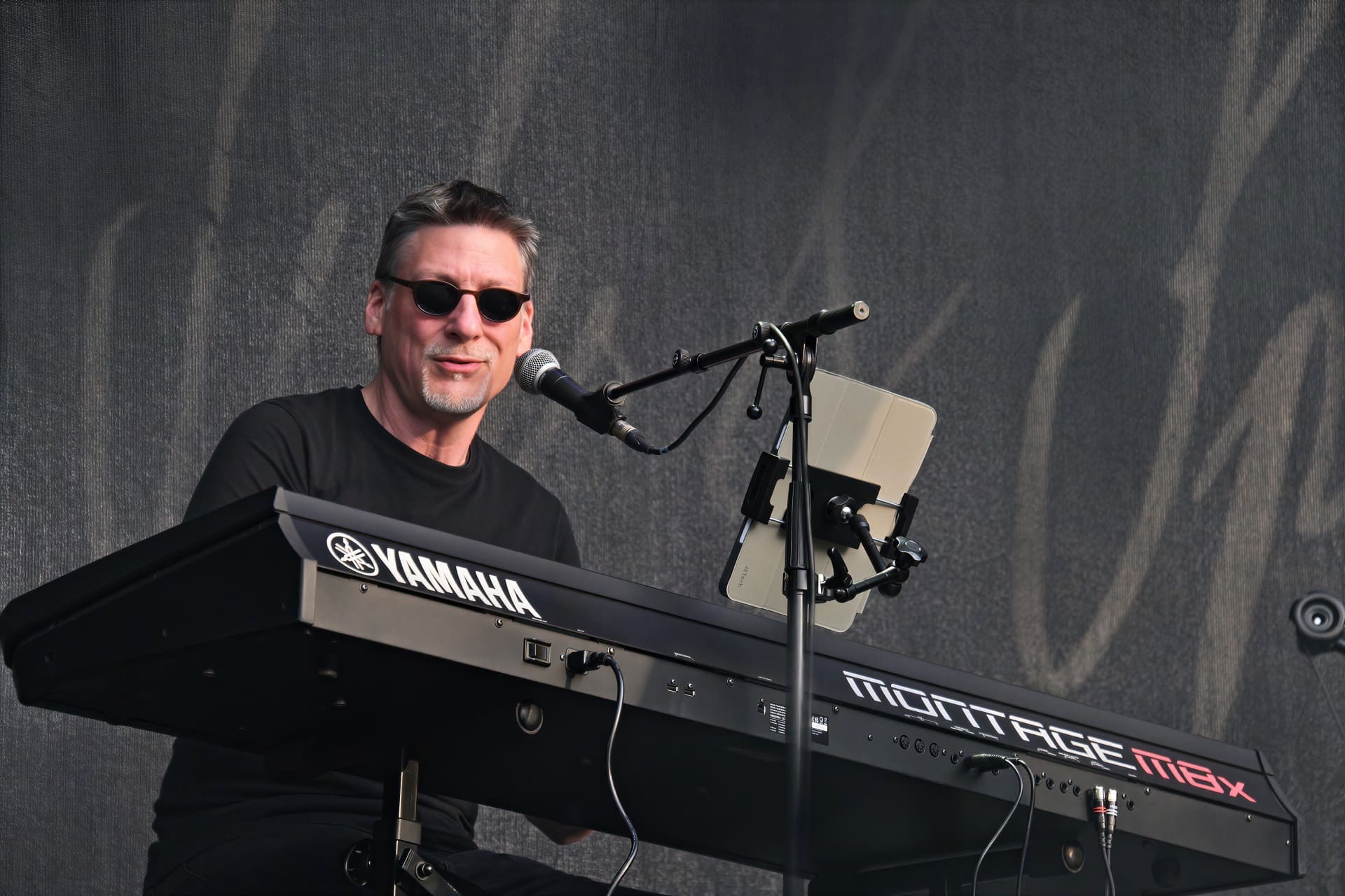 Ein Mann mit Sonnenbrille steht hinter einem Yamaha Keyboard auf der Bühne.