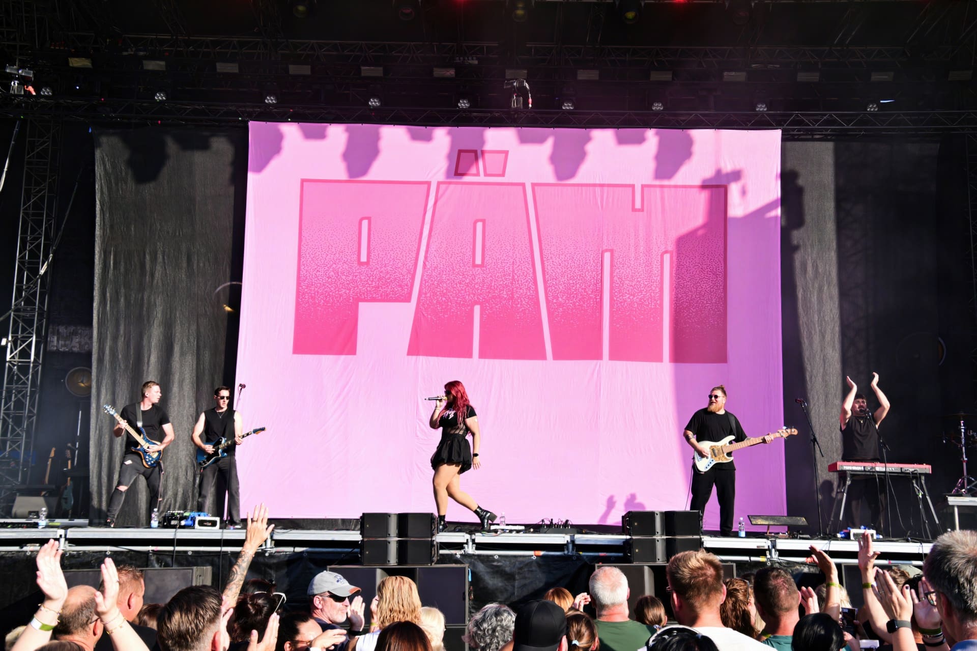 Band PÄM auf der Bühne mit großem pinken Logo und jubelndem Publikum mit erhobenen Händen im Vordergrund.