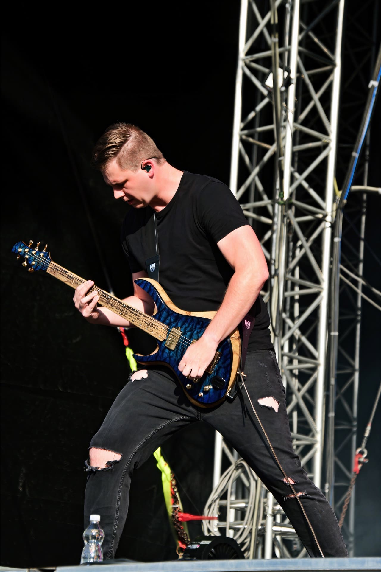 Gitarrist in schwarzem T-Shirt und zerrissener Jeans spielt auf einer Bühne E-Gitarre