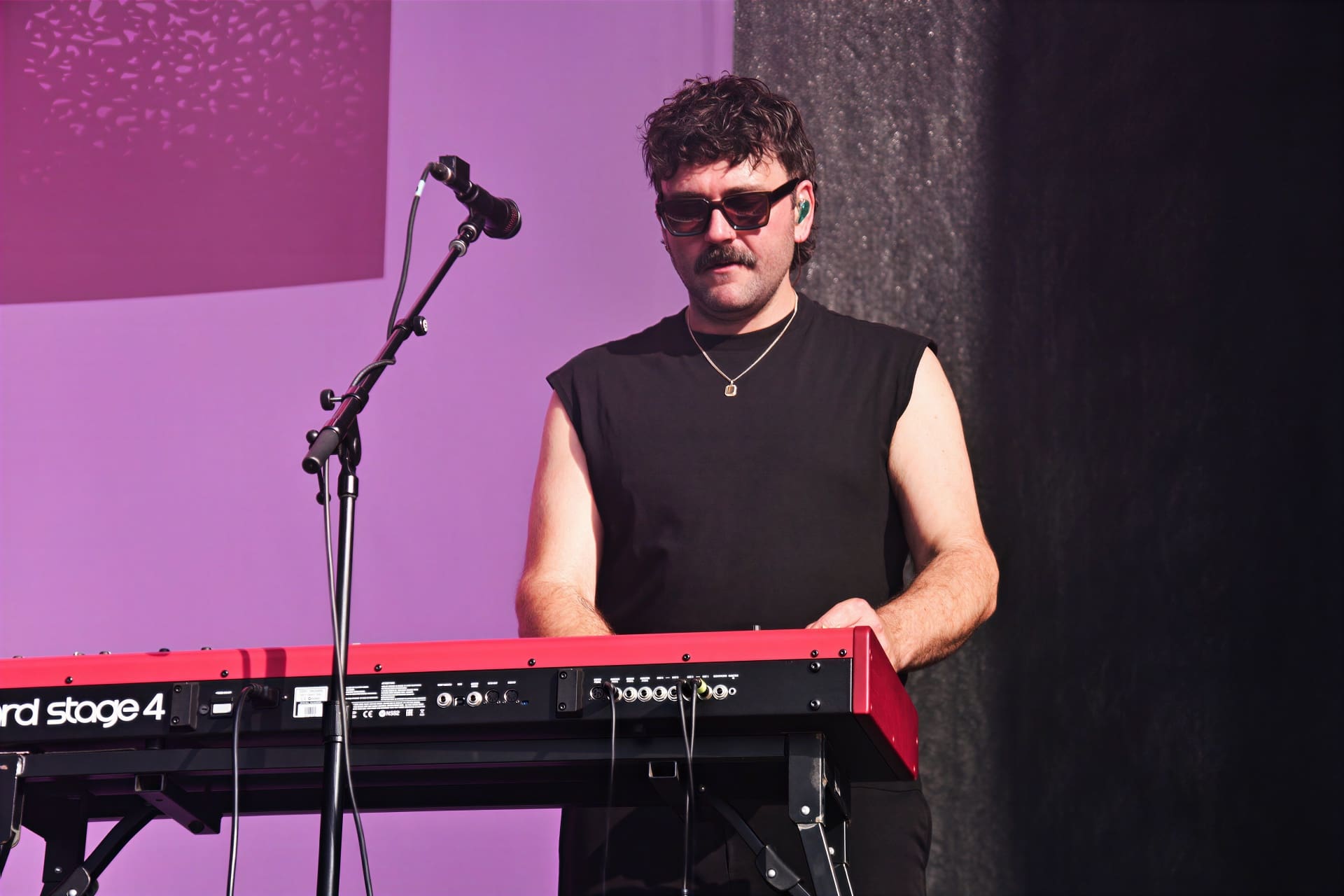 Musiker mit dunklen Locken und Schnurrbart an roter Nord Stage 4 Tastatur auf violetter Bühne