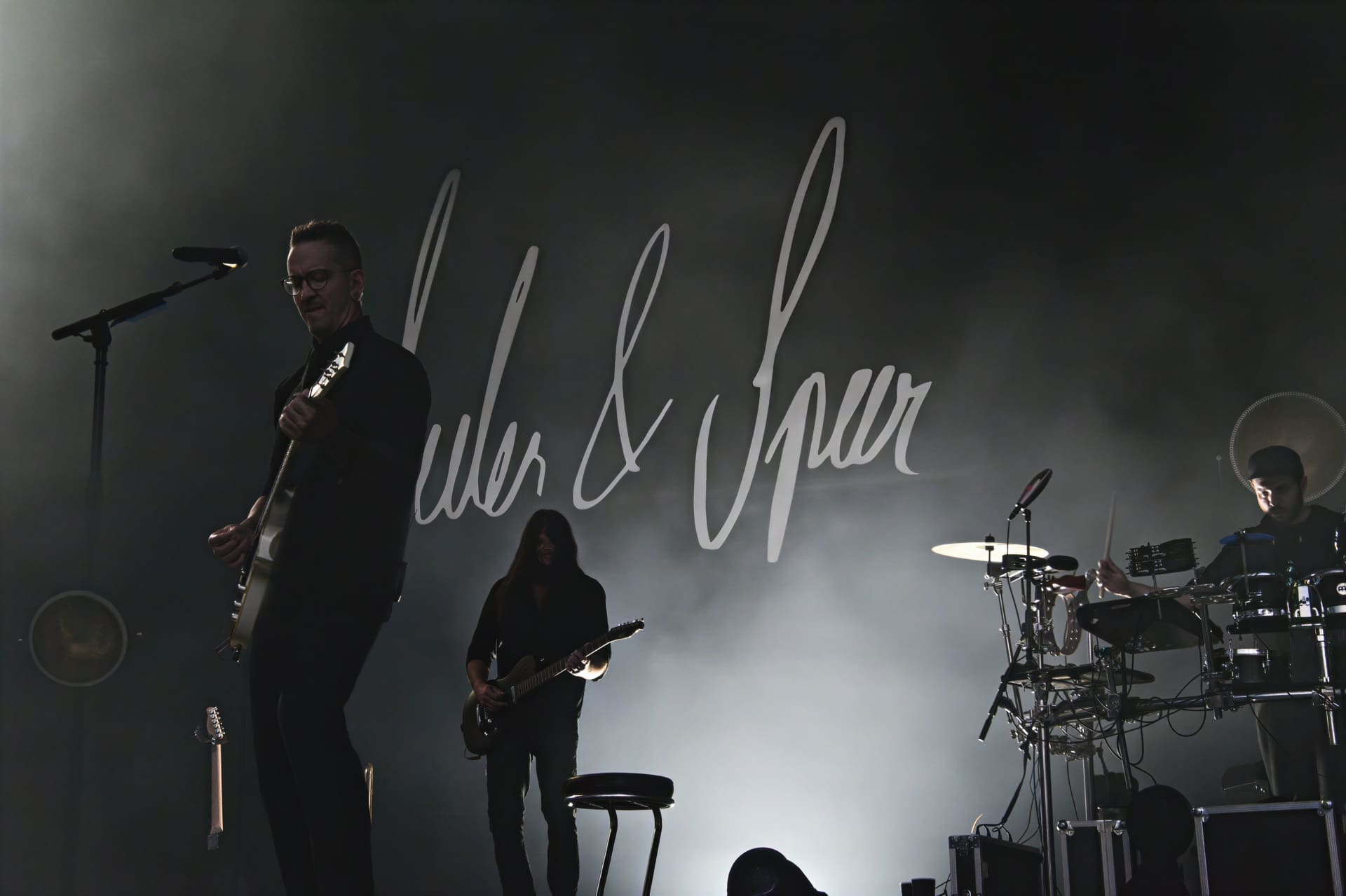 Zwei Gitarristen und ein Schlagzeuger der Band Seiler und Speer auf einer dunklen Bühne mit Logo