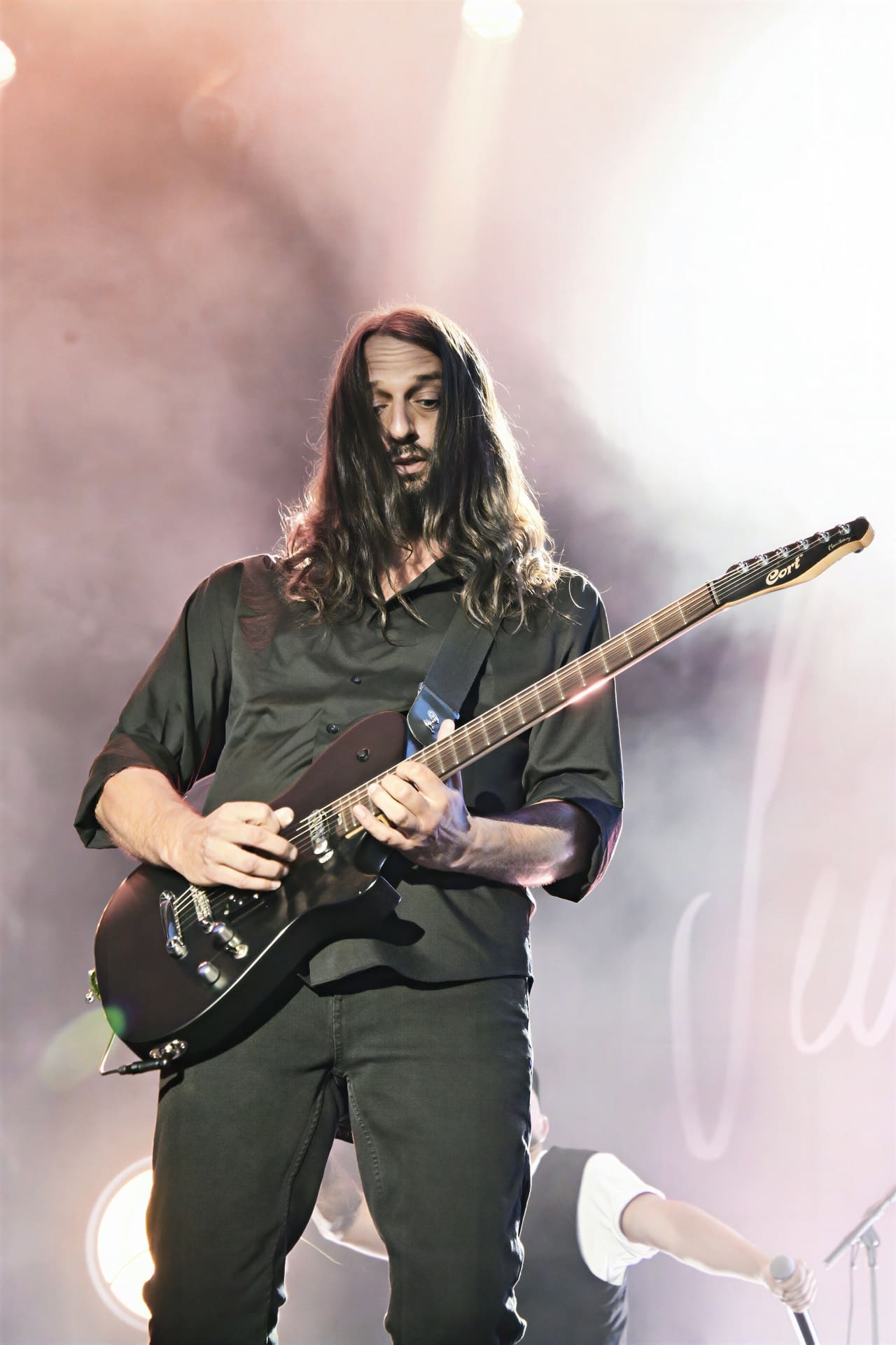 Langhaariger bärtiger Musiker spielt E-Gitarre auf einer beleuchteten Konzertbühne mit Rauch