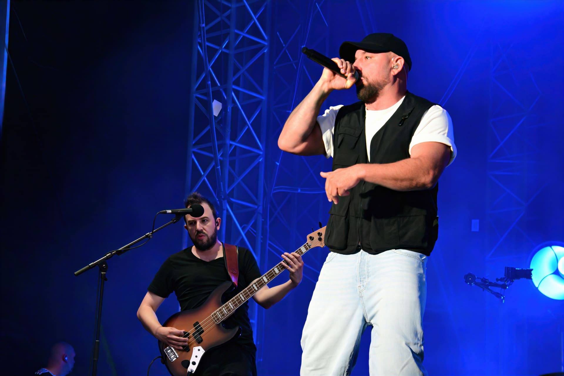 Sänger mit schwarzer Kappe und Bassist auf einer blauen Bühne