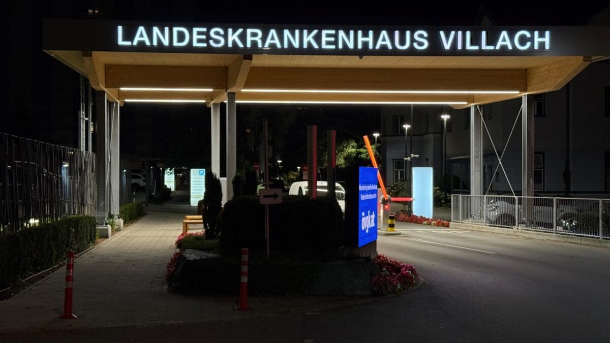 Nächtliche Ansicht des beleuchteten Eingangs zum Landeskrankenhaus Villach mit Parkplatz und Schildern