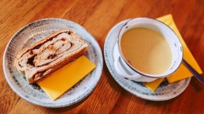 Scheibe Reindling mit Käse auf Keramikteller neben Schüssel mit Suppe auf Holztisch