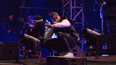 RAF Camora in schwarzer Weste und Cap hockend auf der Bühne mit Bonez MC im Hintergrund