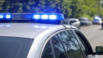 Blaues Blaulicht auf dem Dach eines weißen Polizeiautos mit weiteren Einsatzfahrzeugen im Hintergrund