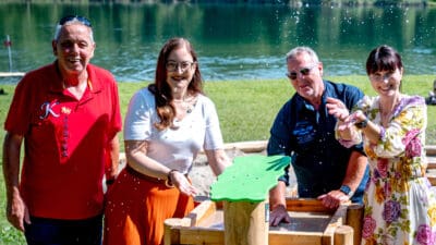 Vier Erwachsene fangen spritzendes Wasser an einem grünen Wasserspielgerät am Seeufer