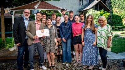 Gruppe von Schülerinnen, Schülern und Erwachsenen steht vor einem Pavillon und lächelt in die Kamera