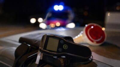 Alkoholtester mit Mundstück liegt vor einem Polizeiauto mit Blaulicht bei Nacht.