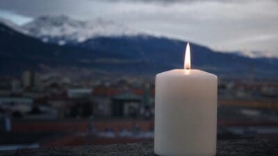 Weiße Kerze brennt auf einer Steinmauer vor einer Stadt und schneebedeckten Bergen