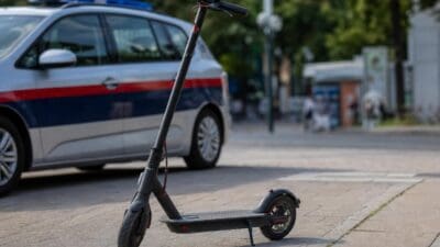 Ein schwarzer E-Scooter steht auf dem Gehweg vor einem Polizeiwagen.