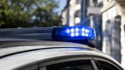 Blaues Blaulicht leuchtet auf dem Dach eines Polizeifahrzeugs vor Gebäuden und Bäumen