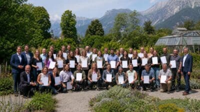 Große Gruppe von Menschen mit weißen Zertifikaten im Botanischen Garten vor Bergkulisse