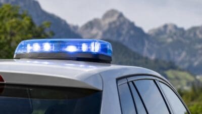 Blaues Blaulicht leuchtet auf dem Dach eines weißen Einsatzfahrzeugs vor einer Berglandschaft in Tirol.