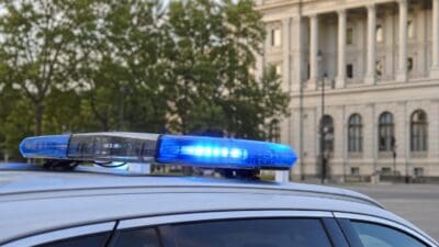 Blaues Blaulicht auf dem Dach eines weißen Polizeifahrzeugs vor einem großen Gebäude