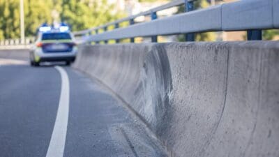 Beschädigte Betonleitwand an einer Brücke mit Polizeiauto und Blaulicht im Hintergrund