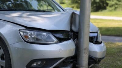 Silbernes Auto mit stark beschädigter Front gegen grauen Metallmast gefahren