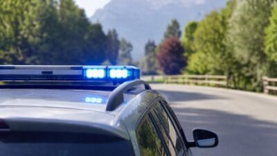 Graues Polizeifahrzeug mit zwei blauen Blaulichtern auf dem Dach vor einer Berglandschaft