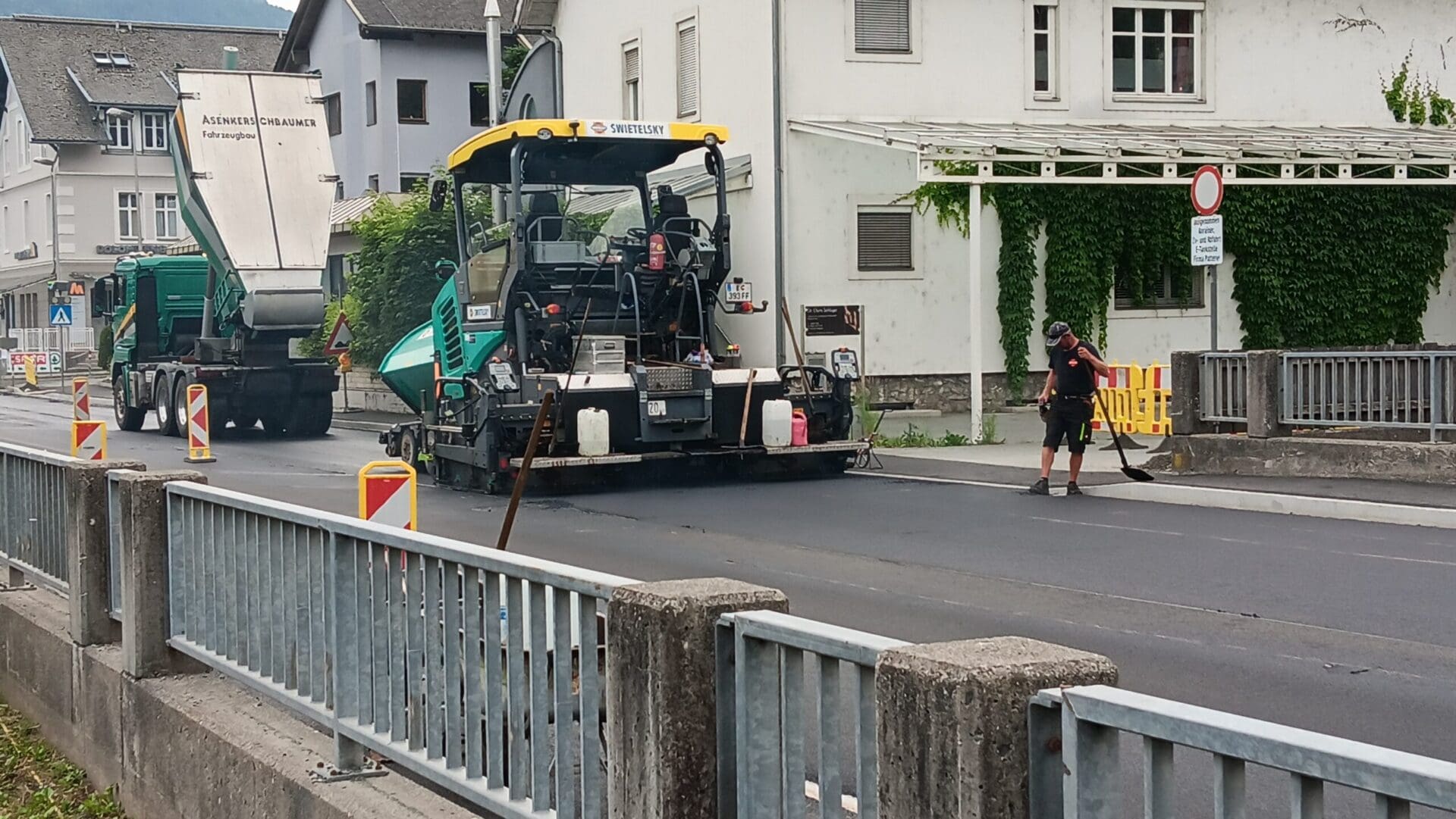 Grün-gelber Asphaltfertiger neben einem Lkw auf einer Baustelle