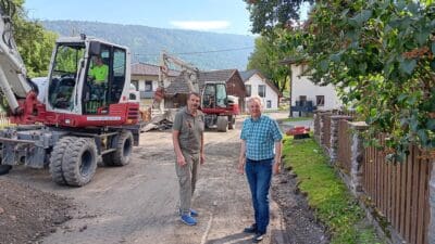 Zwei Männer stehen vor roten und weißen Baggern auf einer Baustelle.