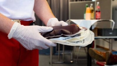 Mitarbeiter hält mit weißen Handschuhen eine Blutkonserve in den Händen