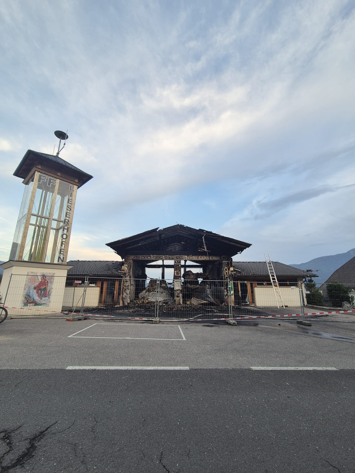 Ausgebranntes Feuerwehrhaus mit dem Schriftzug FF Lieserhofen hinter Absperrgittern unter blauem Himmel
