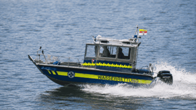 Blaues Rettungsboot der Wasserrettung mit gelben Markierungen und Besatzung auf dem See