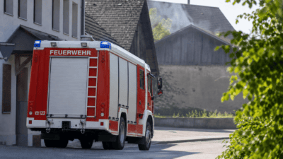 Rückansicht eines roten und weißen Feuerwehrfahrzeugs mit Aufschrift FEUERWEHR auf einer Straße vor Gebäuden
